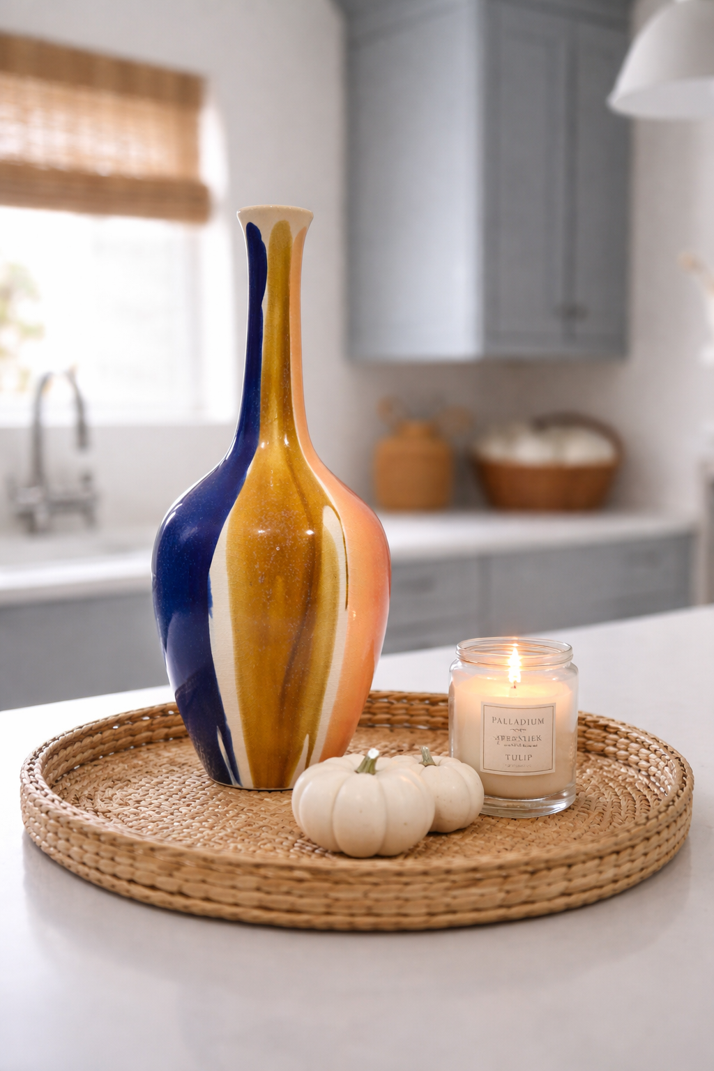 Decorative vase, candles, and pumpkins on a woven tray in a kitchen setting.