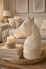 Decorative horse head sculpture on a coffee table with books and a candle in a living room setting.