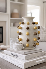 Decorative vase with spherical embellishments on a stack of books in a living room setting