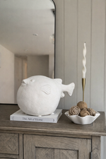Decorative fish sculpture on a book with a candle and decorative items on a wooden surface.