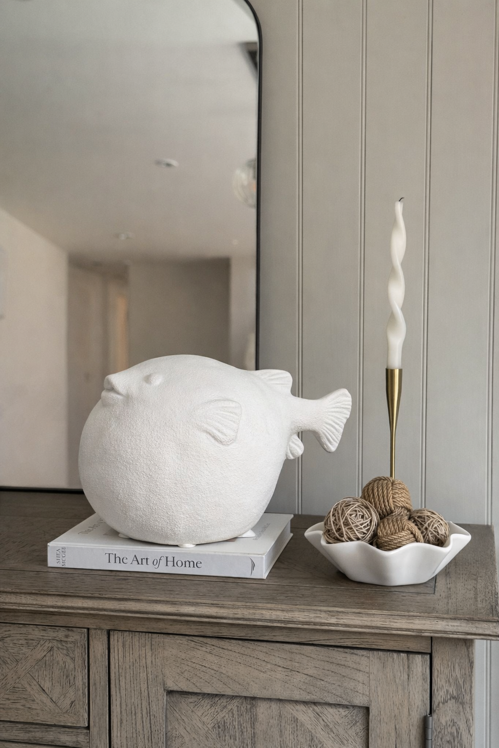 Decorative fish sculpture on a book with a candle and decorative items on a wooden surface.