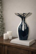 Decorative vase with blue and white abstract pattern on a wooden surface with candles.