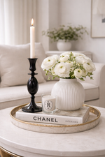 Decorative setting with a vase of white flowers, candle, and book on a coffee table.