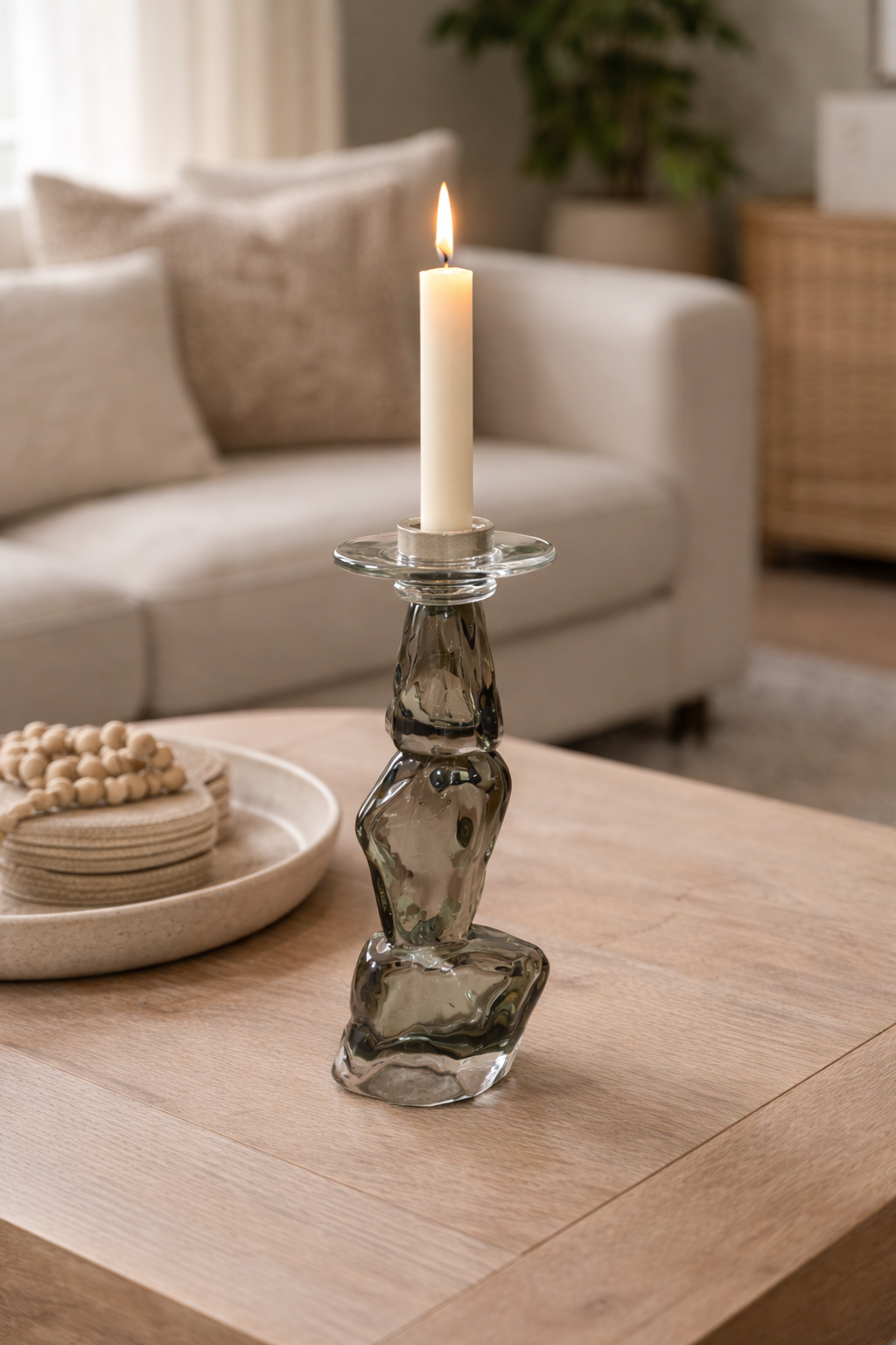 Decorative glass candle holder with a lit candle on a wooden table in a living room setting.
