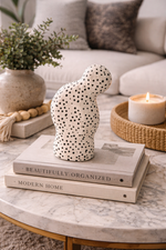 Decorative polka dot vase on books with a candle and plant in the background