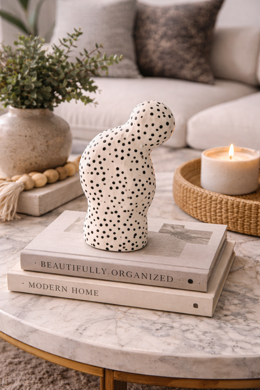 Decorative polka dot vase on books with a candle and plant in the background
