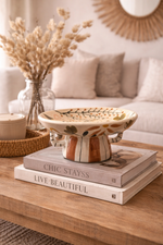 Decorative bowl on books with a vase of dried flowers and a couch in the background