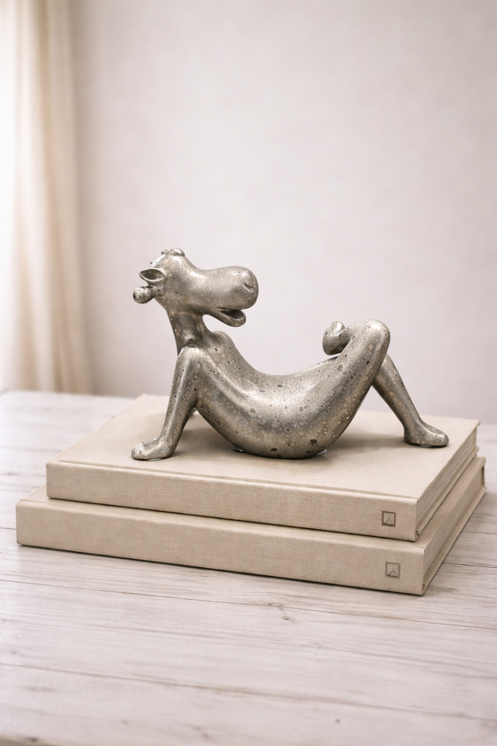 Silver abstract sculpture on a wooden platform against a neutral background
