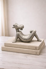 Silver abstract sculpture on a wooden platform against a neutral background