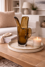 Brown glass vase on a marble tray with a candle, placed on a wooden coffee table in a living room.