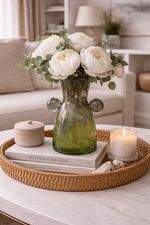 Decorative setting with a vase of white flowers, candles, and books on a tray in a living room.