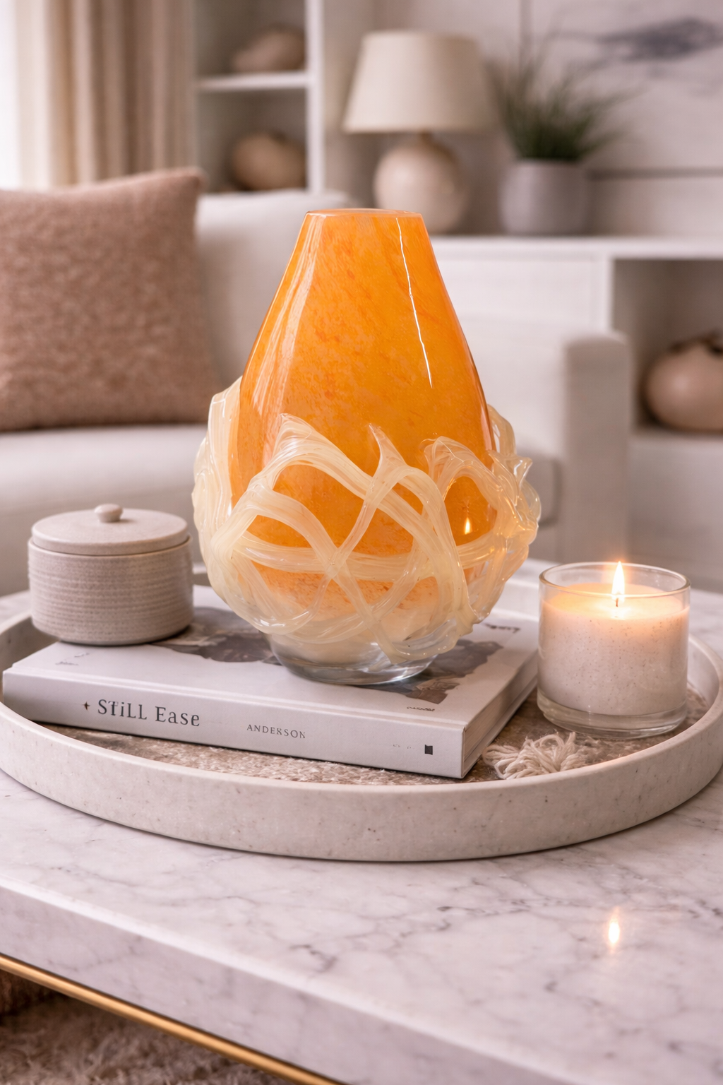 Decorative orange vase with white patterns on a marble surface with candles and books.