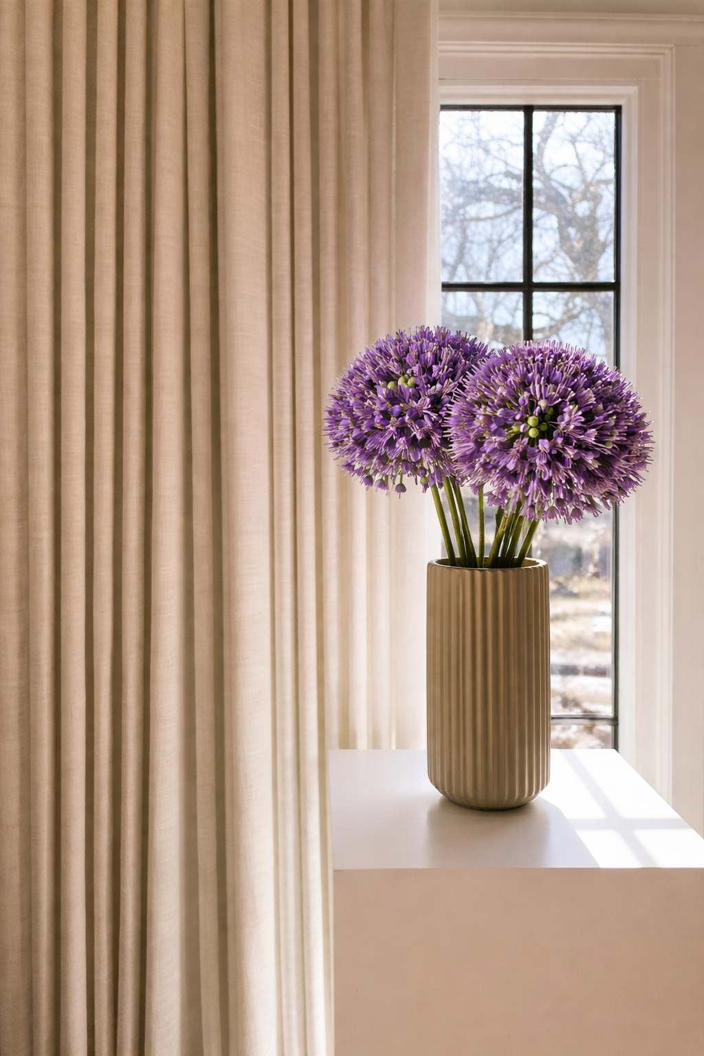 Vase with purple flowers on a windowsill with curtains in the background