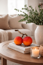 Decorative apples on a wooden table with a candle and plant in the background