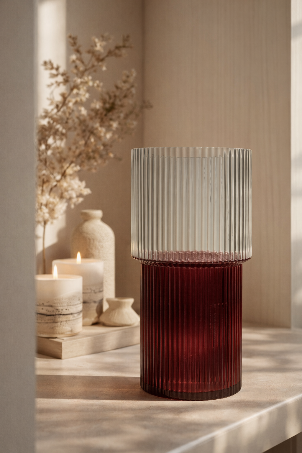 Decorative glass vase with ribbed design on a wooden surface with candles and flowers.