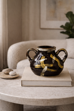 Black ceramic vase with yellow accents on a book on a marble table