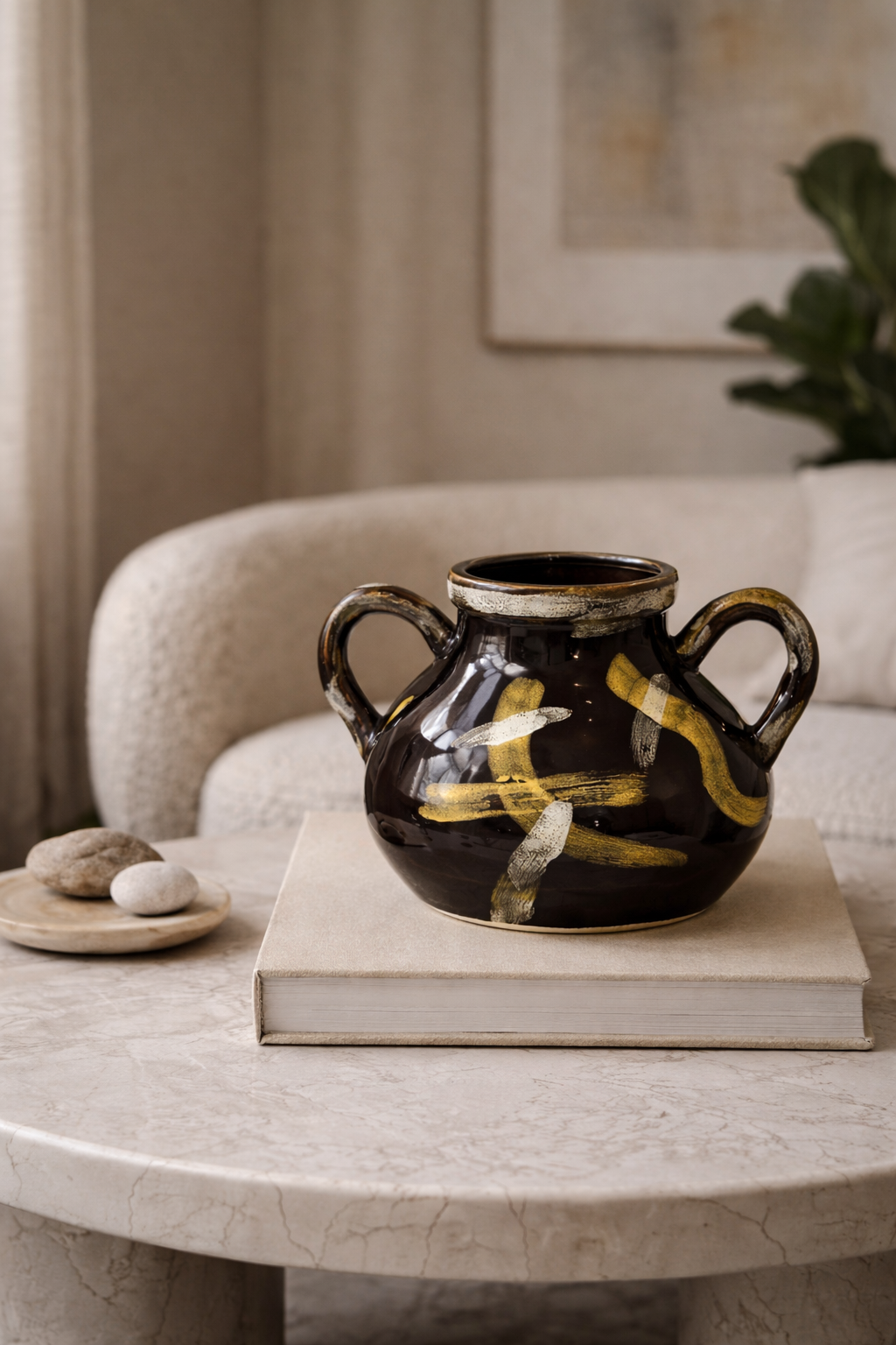 Black ceramic vase with yellow accents on a book on a marble table