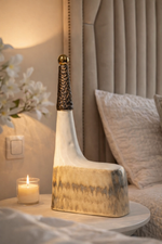 Decorative lamp on a table next to a candle and flowers in a softly lit room.