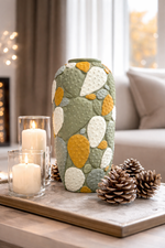 Decorative vase with colorful patterns on a table with candles and pinecones.