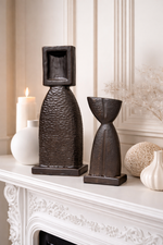 Decorative sculptures on a mantelpiece with a candle and other items.