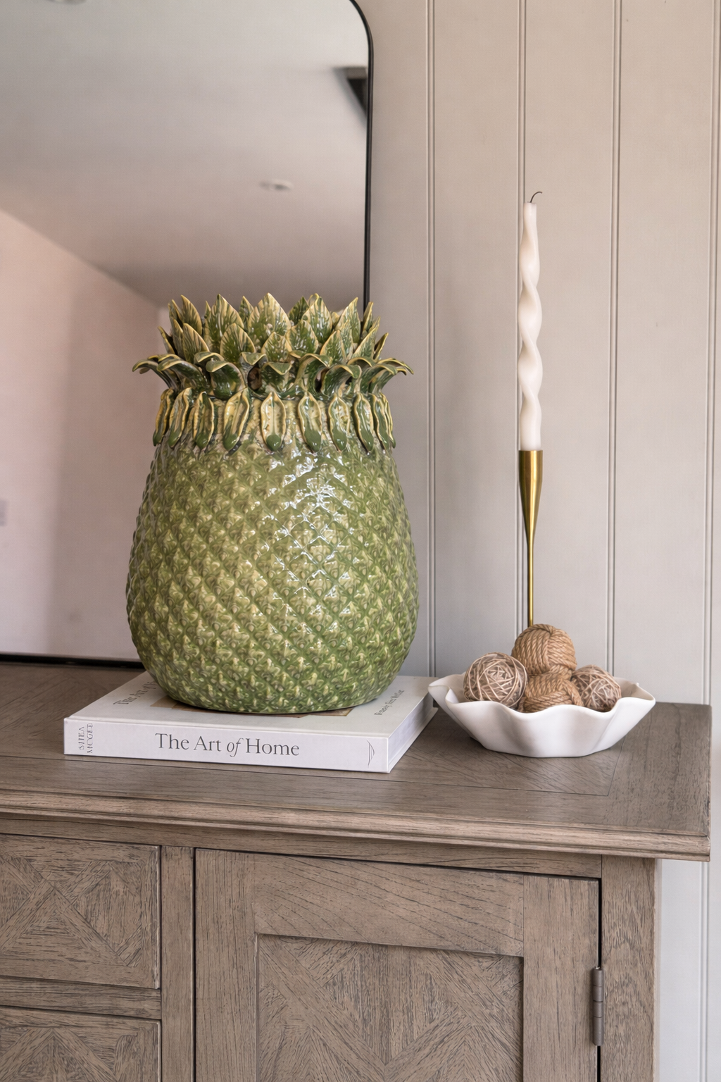 Decorative pineapple on a book with a candle and small items on a wooden surface.