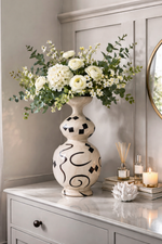 Decorative vase with flowers on a dresser against a neutral wall.