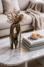 Decorative vase with dried flowers on a marble coffee table with books and a candle.