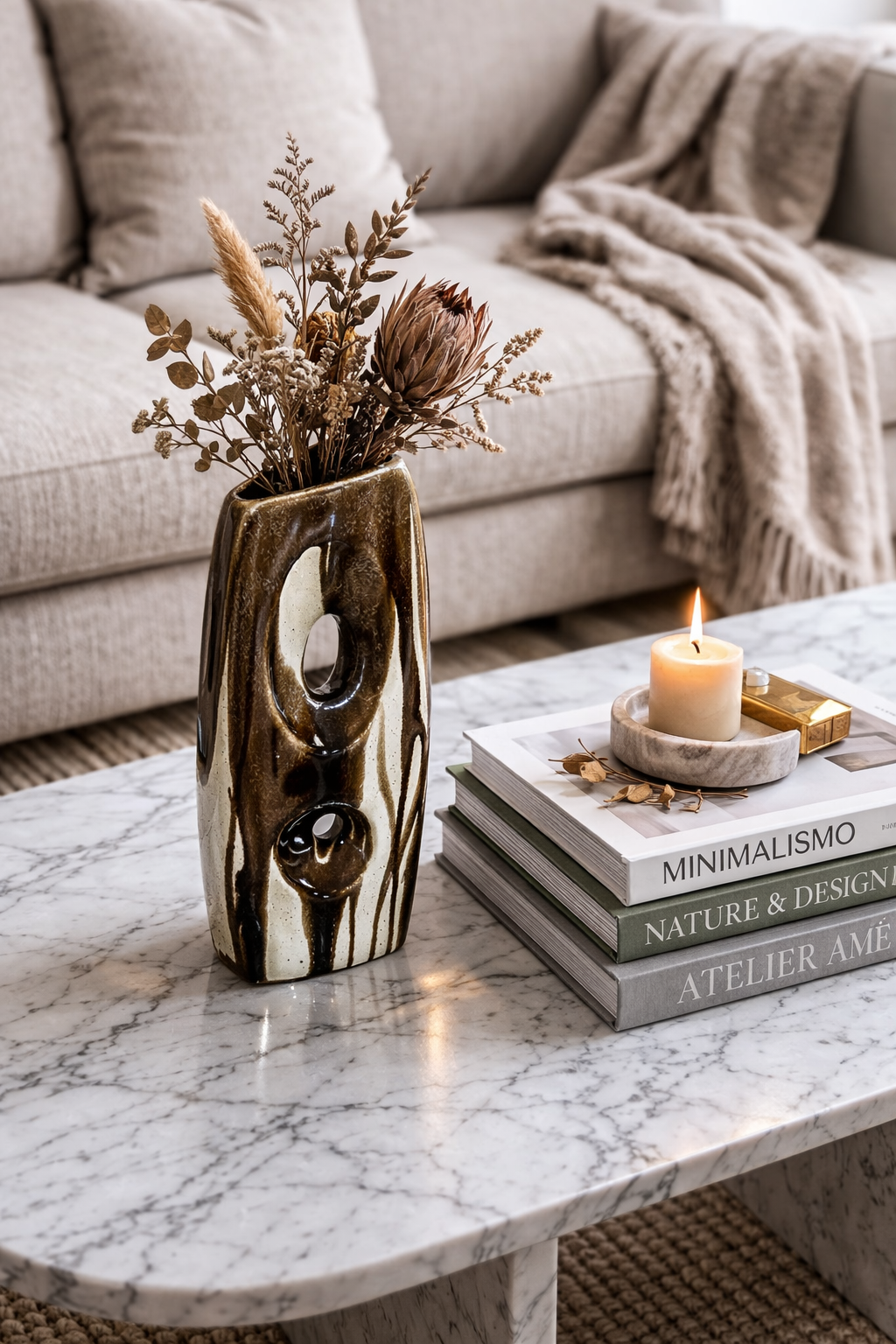 Decorative vase with dried flowers on a marble coffee table with books and a candle.
