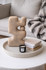 Decorative sculpture on a round tray with books and a candle, placed on a coffee table.