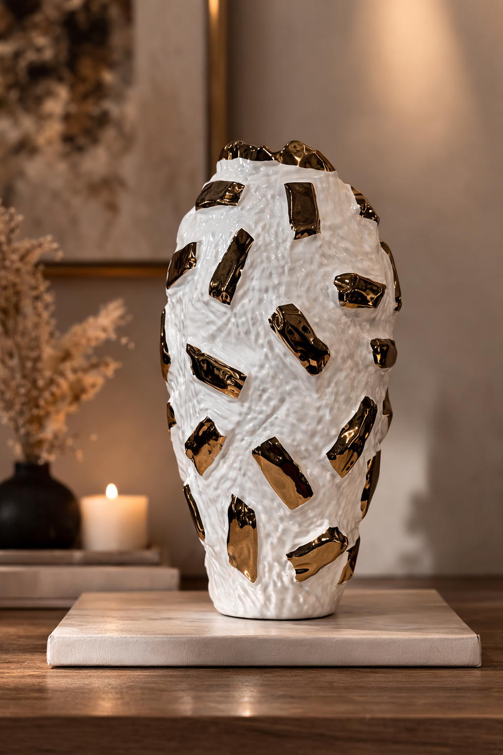 Decorative vase with gold accents on a wooden surface with a candle and plant in the background.