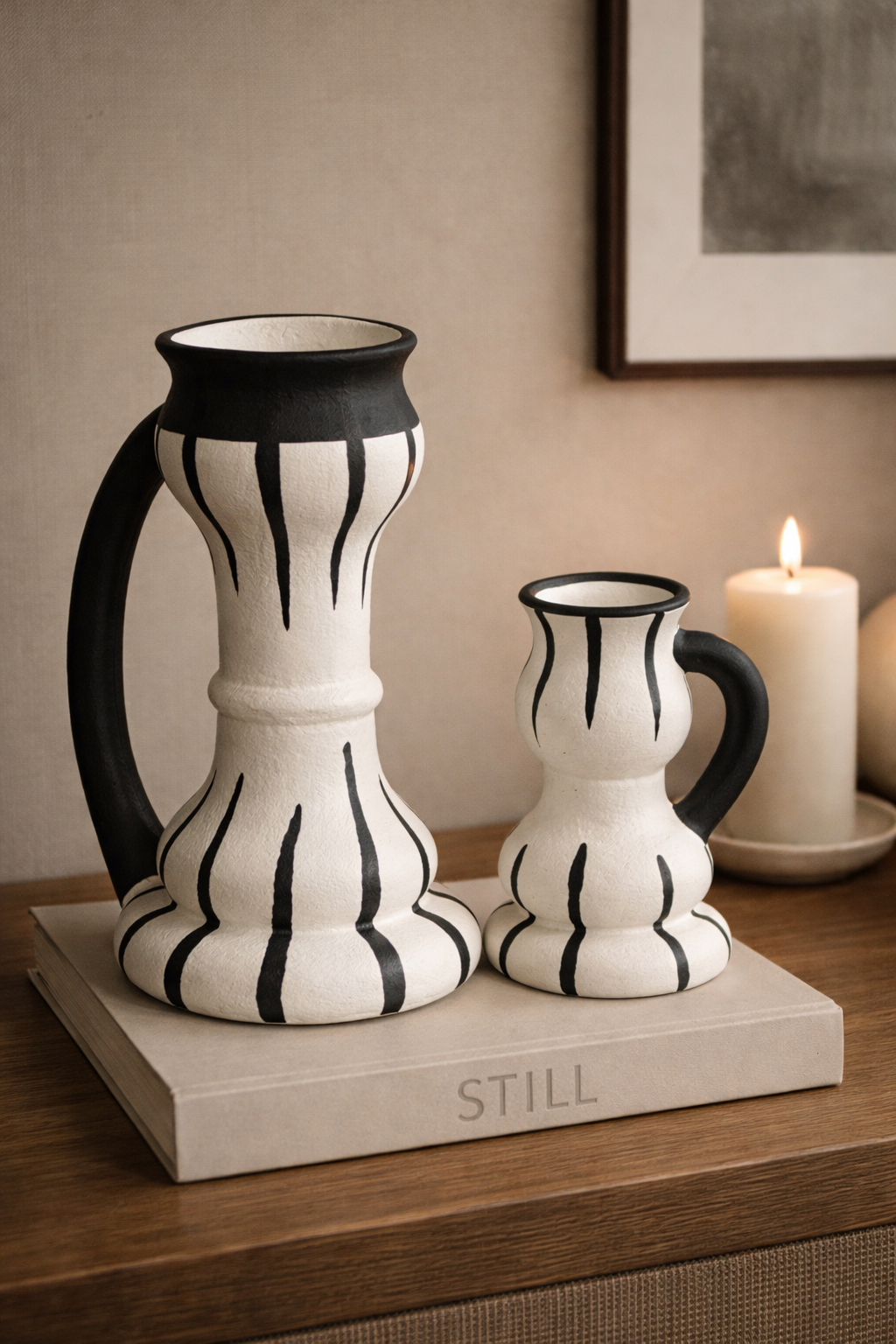 Two black and white striped vases on a wooden surface with a candle in the background.