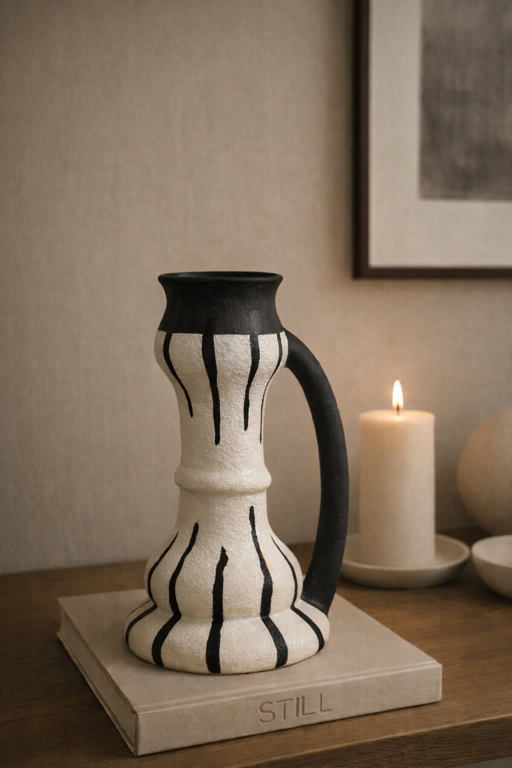 Ceramic pitcher with black and white design on a wooden surface, candle in the background