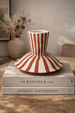 Ceramic vase with red and white stripes on a stack of books titled 'The Kinfolk Home' and 'Robert Amsterdam'.