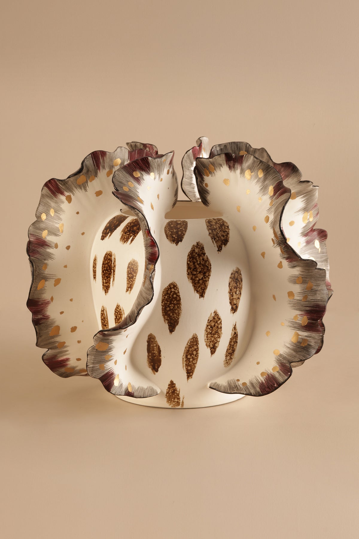 Decorative ceramic plate with scalloped edge and brown speckled pattern on a beige background