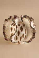Decorative ceramic plate with scalloped edge and brown speckled pattern on a beige background