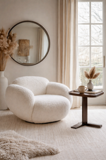 White armchair in a stylish living room with a round mirror and small table.