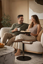 Man and woman sitting on a couch, man reading a book and holding a mug, woman looking at him.
