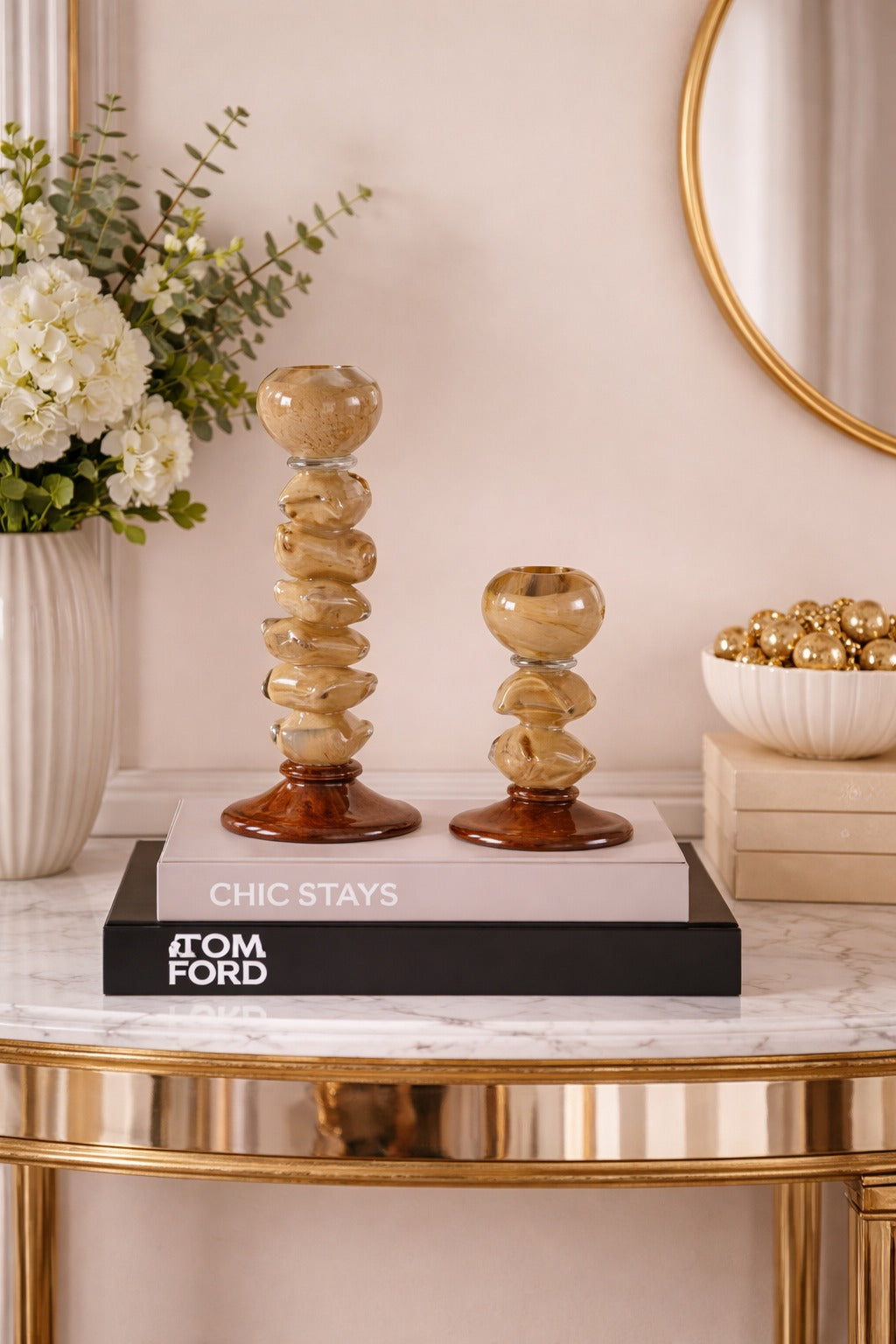 Decorative candle holders on a book with 'Tom Ford' branding, placed on a marble surface with a floral arrangement in the background.